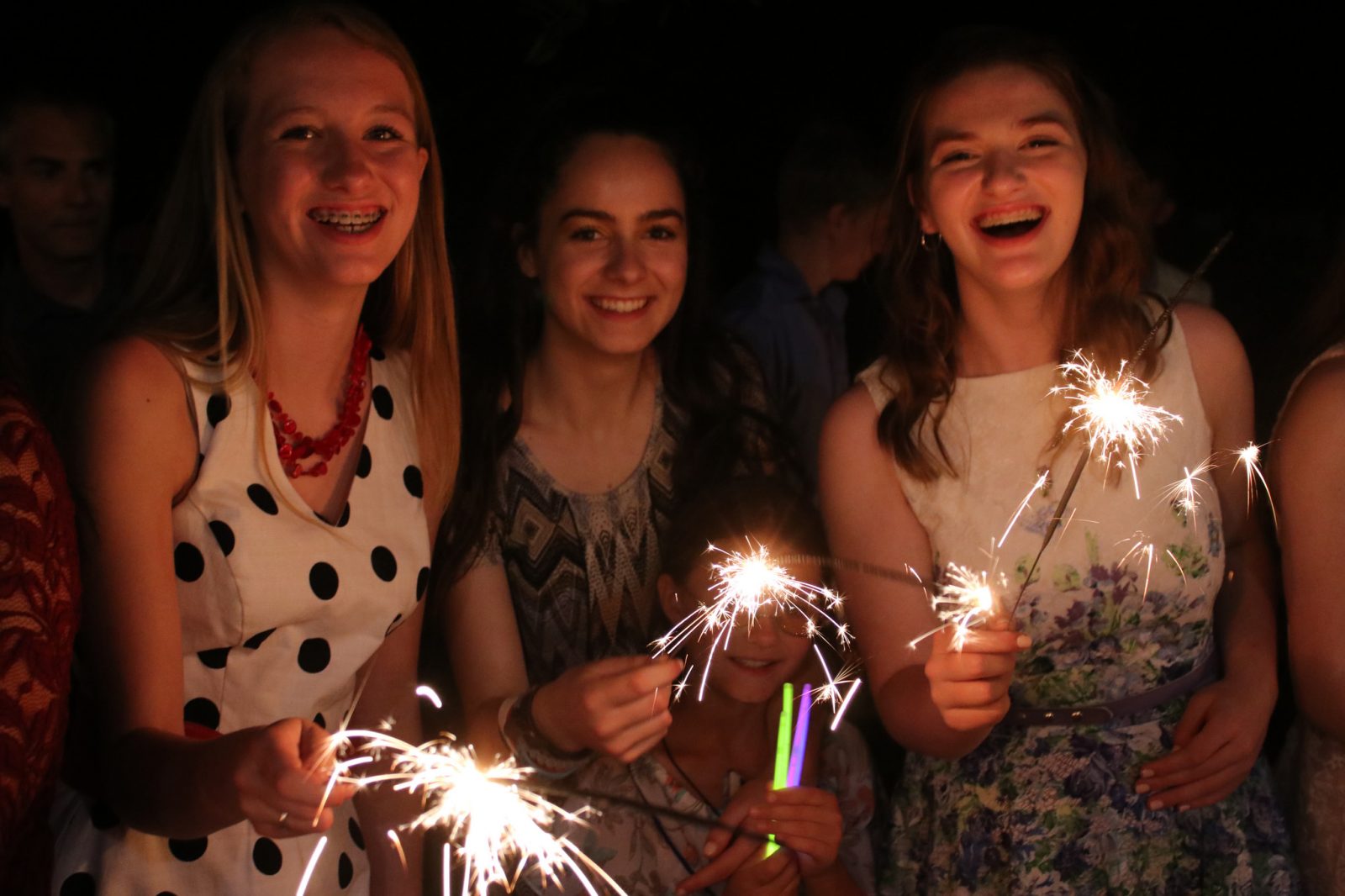 Smiling online Christian homeschooling students are gently illuminated by sparklers at a celebration